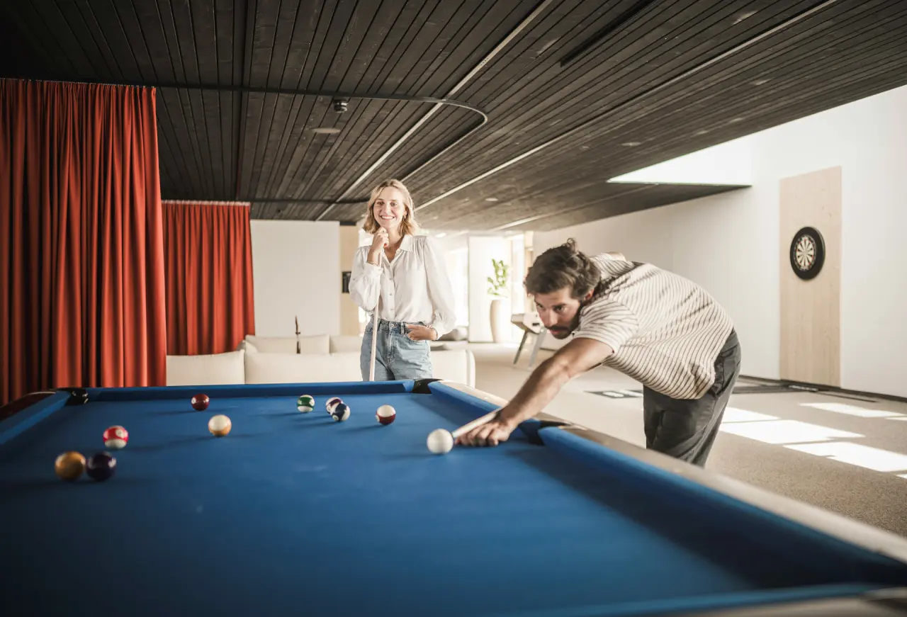 Gäste spielen Billard in der Lounge der Sportlers Lodge Sölden mit Dartscheibe im Hintergrund.