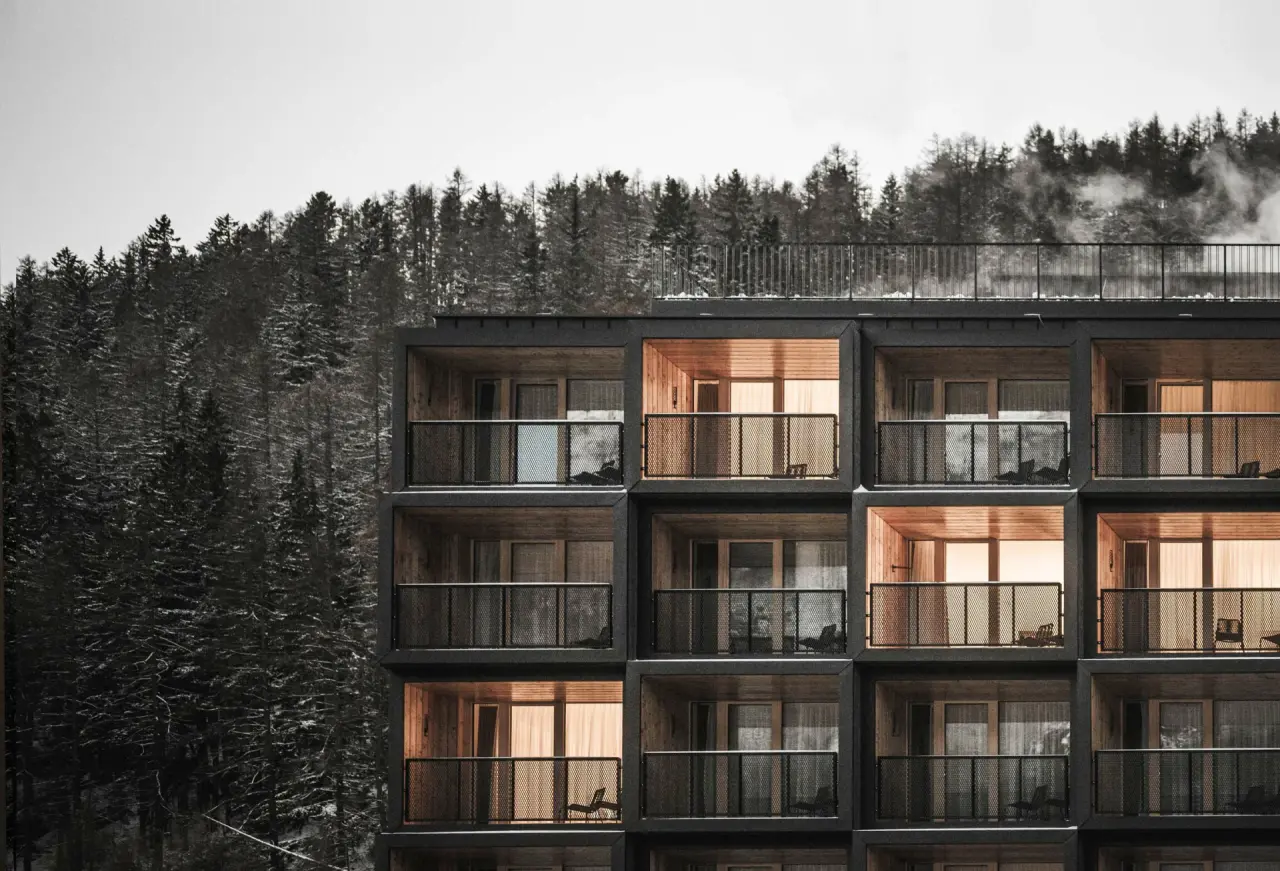Moderne Architektur der Sportlers Lodge Sölden im Winterwald mit beleuchteten Balkonen und Bergblick.