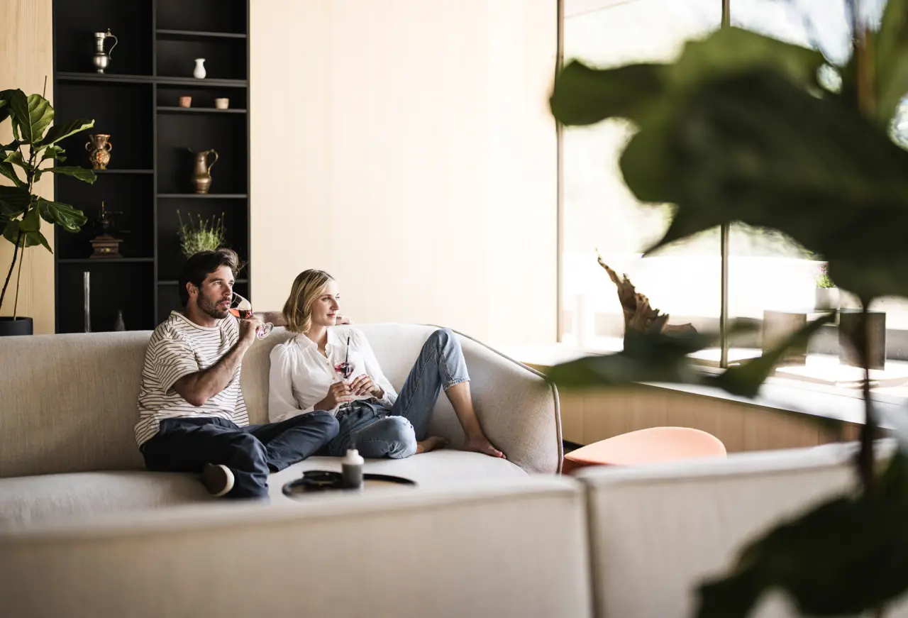 Paar entspannt auf einem Sofa in der modernen Lobby der Sportlers Lodge Sölden mit Blick ins Grüne.