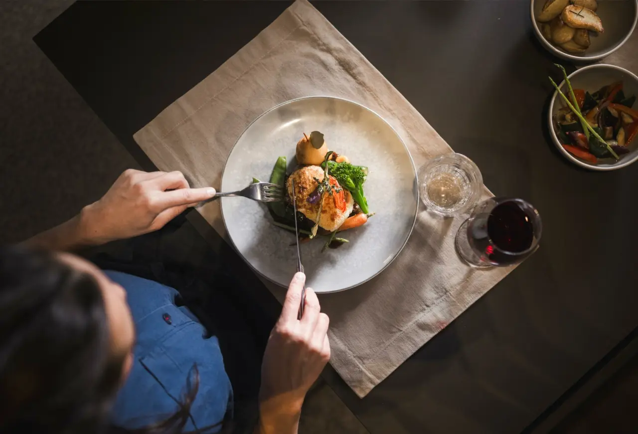 Gast genießt ein exquisites Gericht mit Gemüse und Rotwein im Restaurant der Sportlers Lodge Sölden.