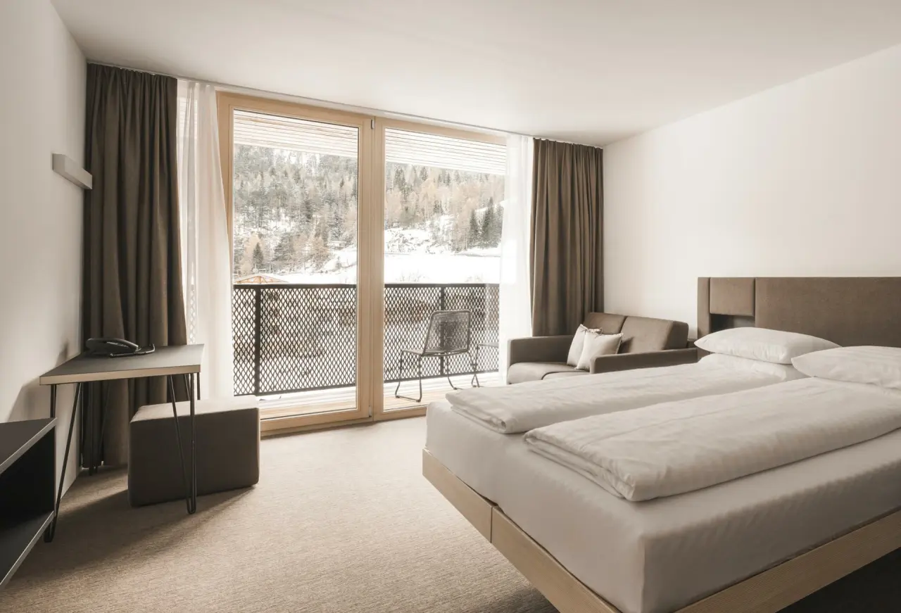 Modernes Hotelzimmer mit Doppelbett, Sofa und Balkon mit Blick auf verschneite Landschaft im Sportlers Lodge Sölden.