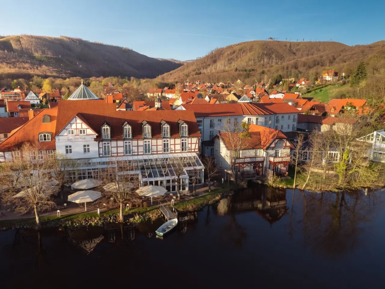 Luftaufnahme des Landhaus Zu den Rothen Forellen am Wasser mit traditioneller Architektur und bewaldeten Hügeln im Harz.