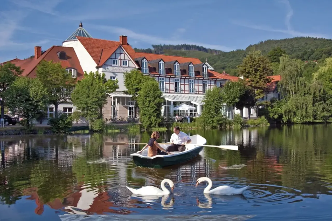 Landhaus Zu den Rothen Forellen am See mit Ruderboot, Paar und Schwänen. Malerische Hotel-Aussenansicht in idyllischer Natur.