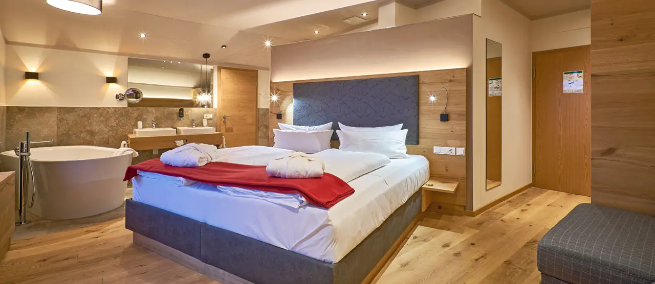Geräumiges Hotelzimmer im Wellnesshotel Zum Koch mit freistehender Badewanne, Doppelbett und Holzelementen.