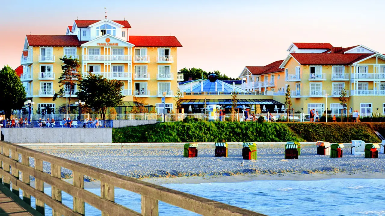 Travel Charme Ostseehotel Kühlungsborn: Strandlage mit Hotelgebäude, Seebrücke und bunten Strandkörben an der Ostsee.