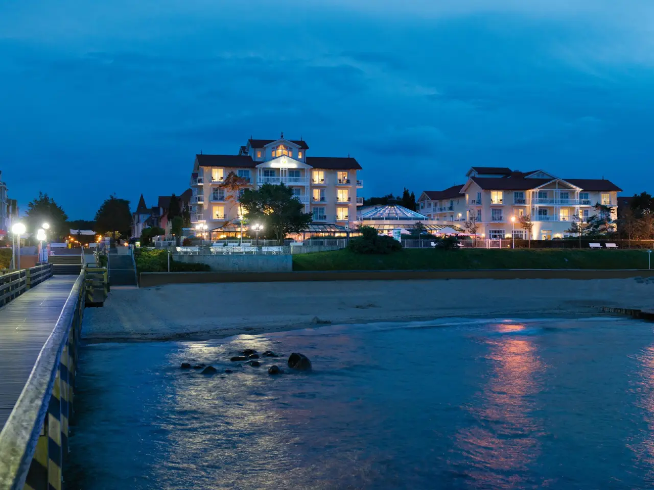Abendansicht des Travel Charme Ostseehotel Kühlungsborn mit beleuchteter Seebrücke und Strand an der Ostsee.