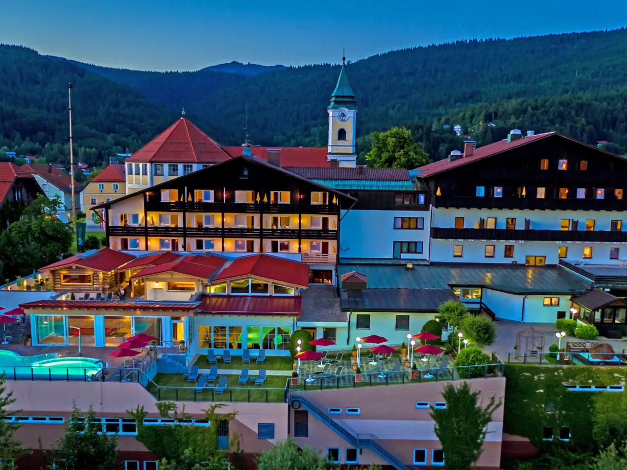 Abendliche Aussenansicht des Wellnesshotel Hofbräuhaus mit beleuchtetem Pool und Bergpanorama.