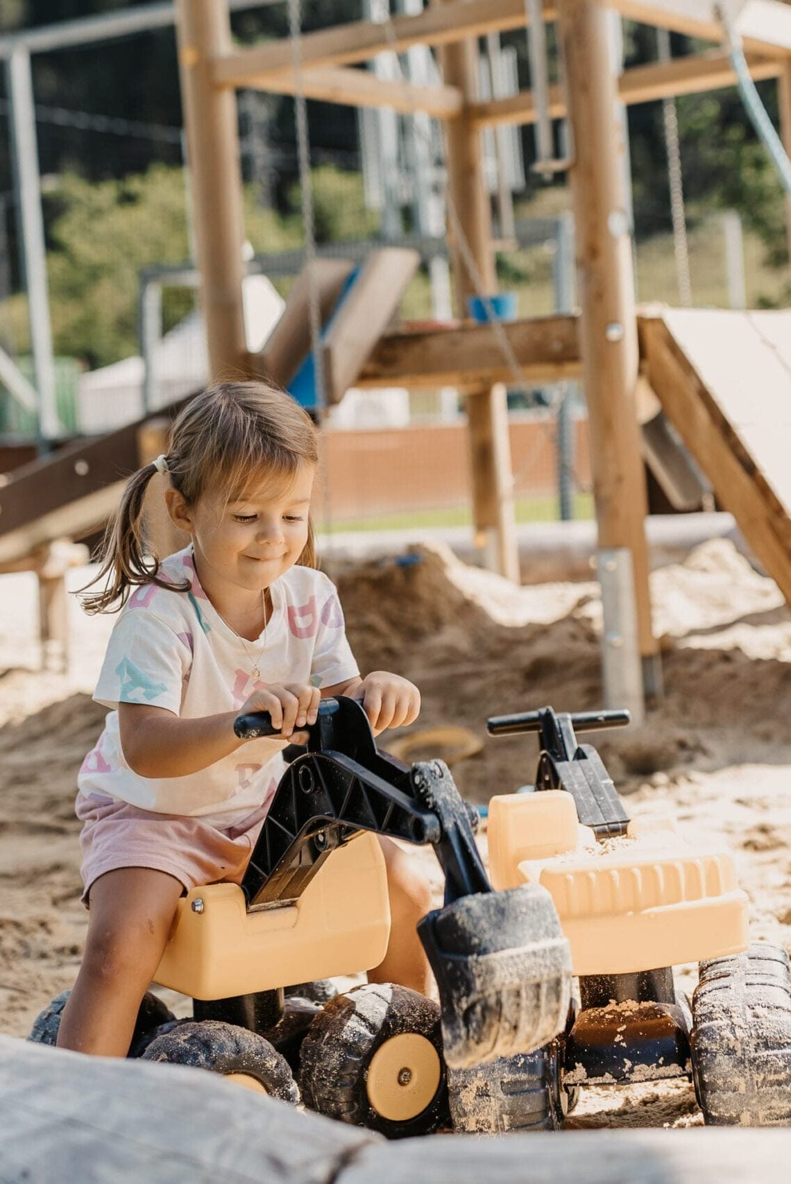 Hofgut Apartment & Lifestyle Resort Wagrain in Wagrain – Lächelndes Kind spielt mit Bagger im Sand auf dem Spielplatz | Wellnesshotel Salzburger Land