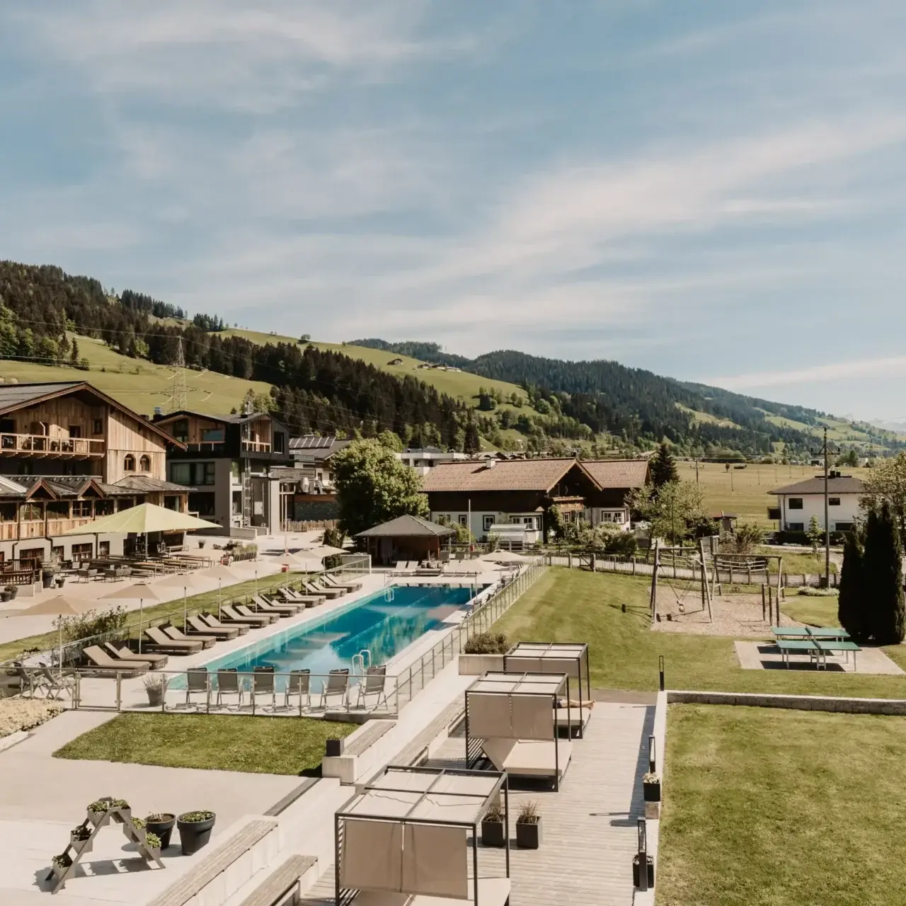 Grosser Aussenpool mit Liegen und Cabanas im Hofgut Apartment & Lifestyle Resort Wagrain, umgeben von grünen Hügeln.