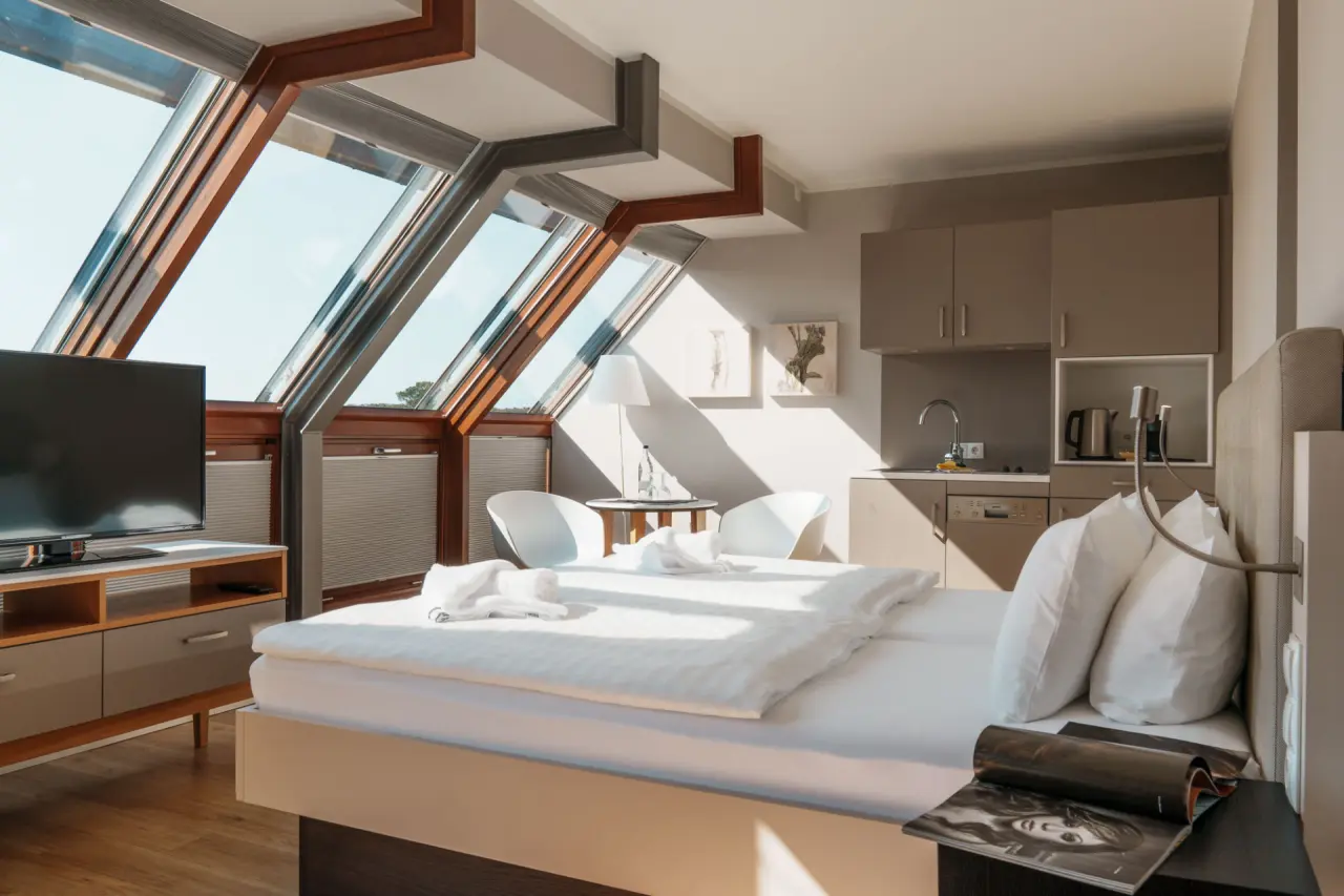 Helles Dachzimmer im Hotel meerSinn Binz mit Doppelbett, moderner Küchenzeile und großen Dachfenstern für viel Tageslicht.
