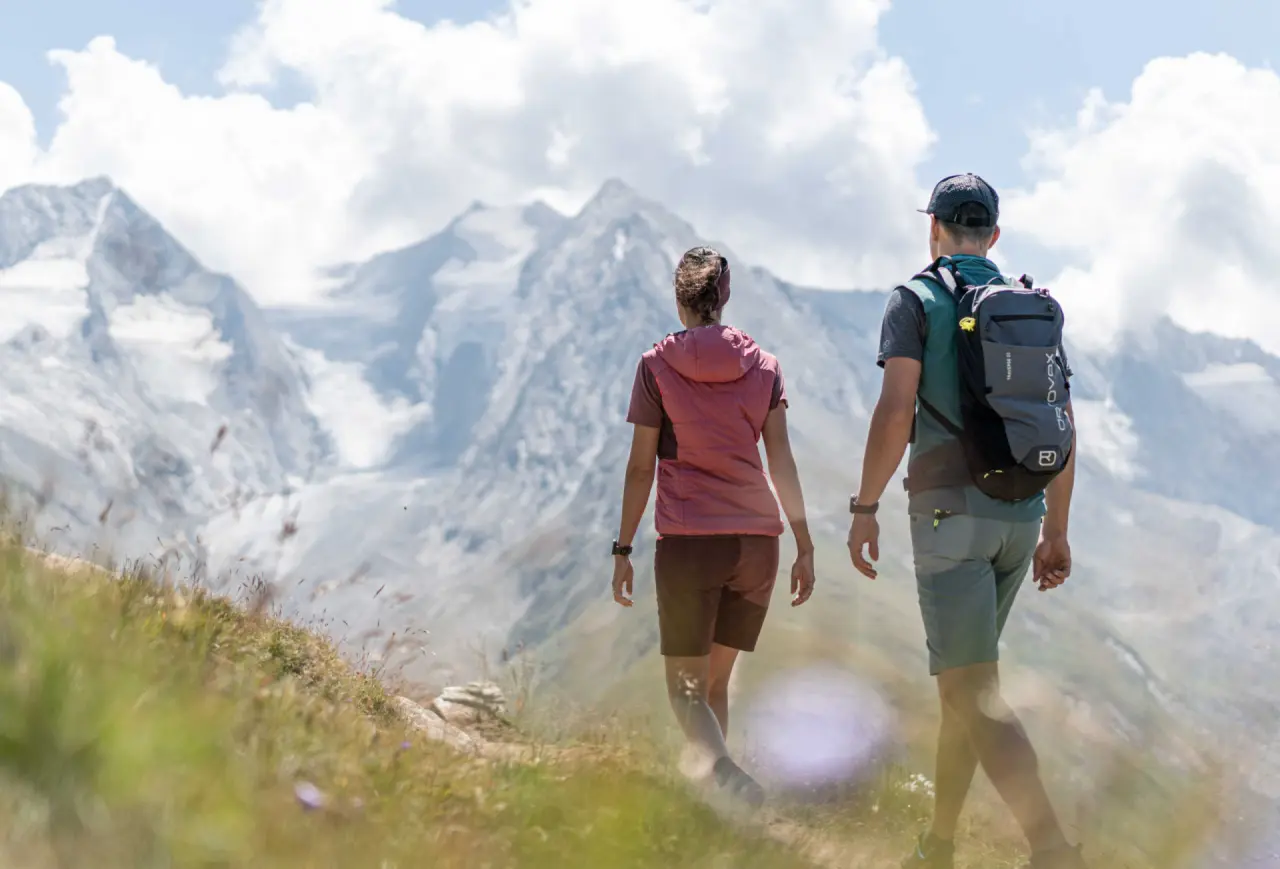 Wandererpaar mit Rucksäcken auf einem Bergpfad mit Blick auf die Gletscher der Alpen, nahe dem Aparthotel Grünwald Resort Sölden.