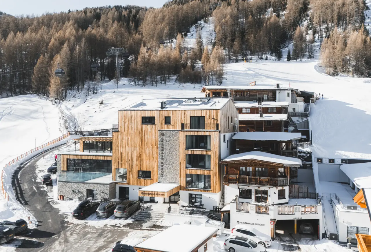 Aparthotel Grünwald Resort Sölden im Winter: Modernes Gebäude am Hang, umgeben von Schnee, Wald und Skipisten mit Gondelbahn.