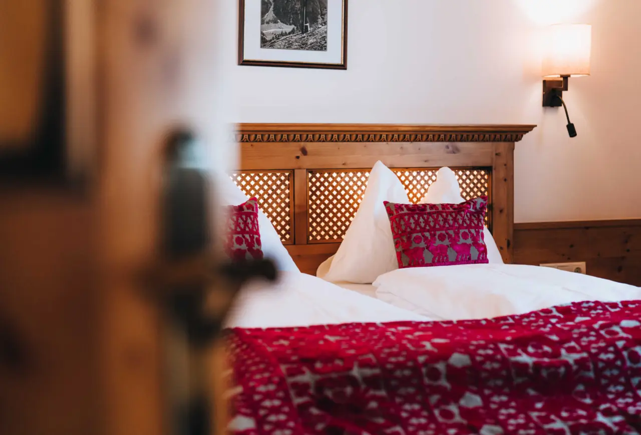 Gemütliches Doppelbett mit Holzkopfteil und roten Akzenten im Aparthotel Grünwald Resort Sölden.