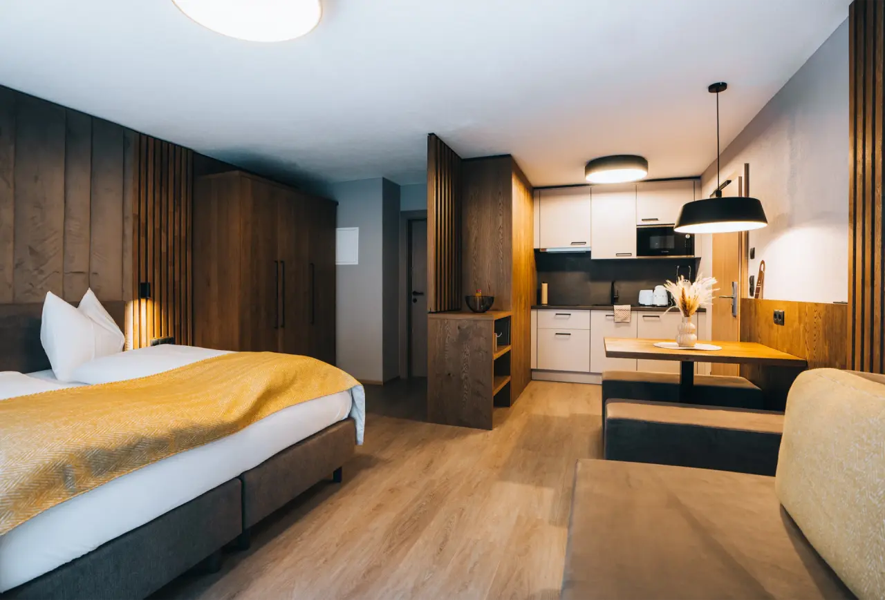 Modernes Apartment im Aparthotel Grünwald Resort Sölden mit Doppelbett, Küchenzeile und Essbereich.