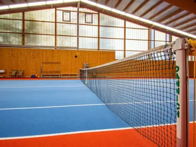 Indoor-Tennisplatz mit blau-orangefarbenem Boden und Netz im Vital- und Wellnesshotel Albblick.