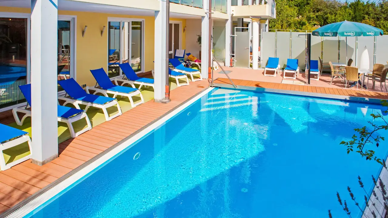 Sonniger Aussenpoolbereich mit blauen Liegestühlen und Holzdeck im Vital- und Wellnesshotel Albblick.