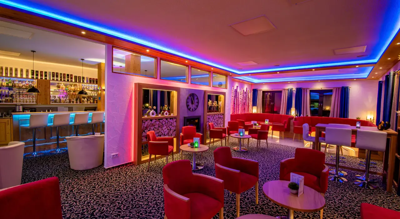 Moderne Hotelbar mit blauer LED-Beleuchtung und roten Sesseln im Vital- und Wellnesshotel Albblick.