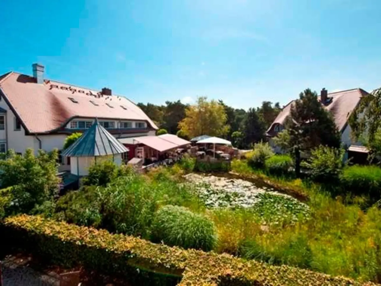 Aussenansicht des Fürst Jaromar Resort & Spa mit traditionellen Gebäuden, üppigem Garten und Seerosenteich unter blauem Himmel.