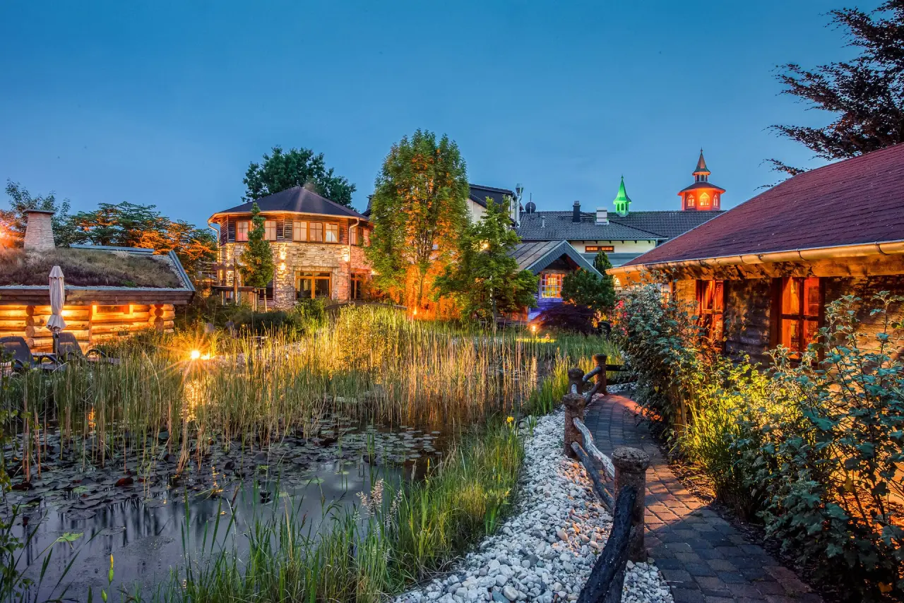 Romantische Abendstimmung im Wellnesshotel Seeschlösschen: beleuchtete Gebäude, Naturteich und Saunahütte im Gartenbereich.