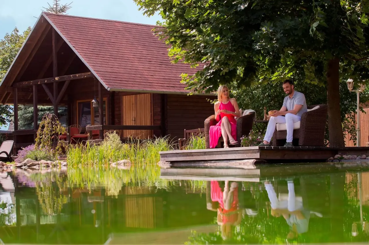 Paar entspannt am Naturteich mit Holzhaus im Hintergrund im Garten des Wellnesshotel Seeschlösschen.