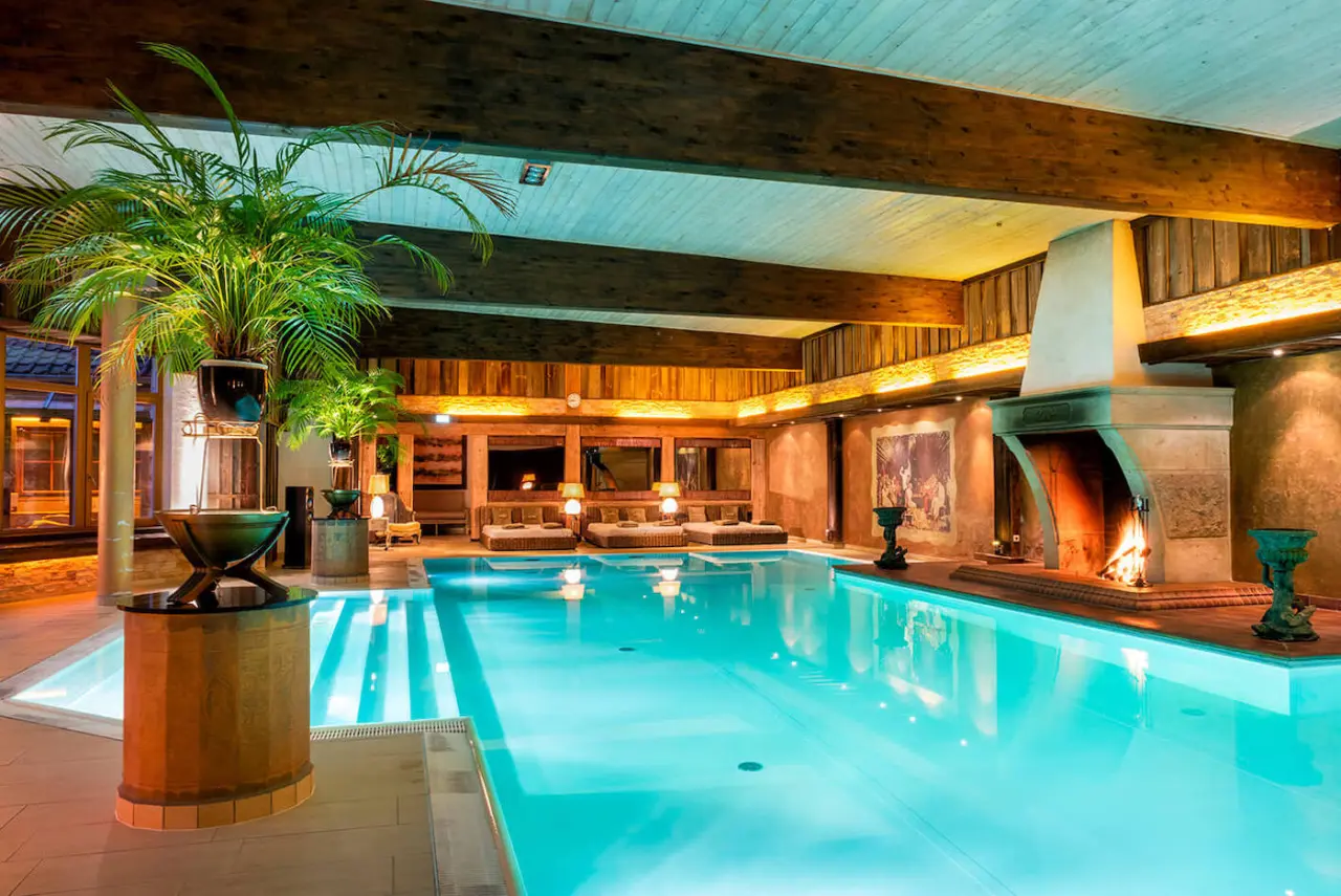 Luxuriöser Innenpool mit Kamin, Palmen und Entspannungsliegen im Wellnesshotel Seeschlösschen.