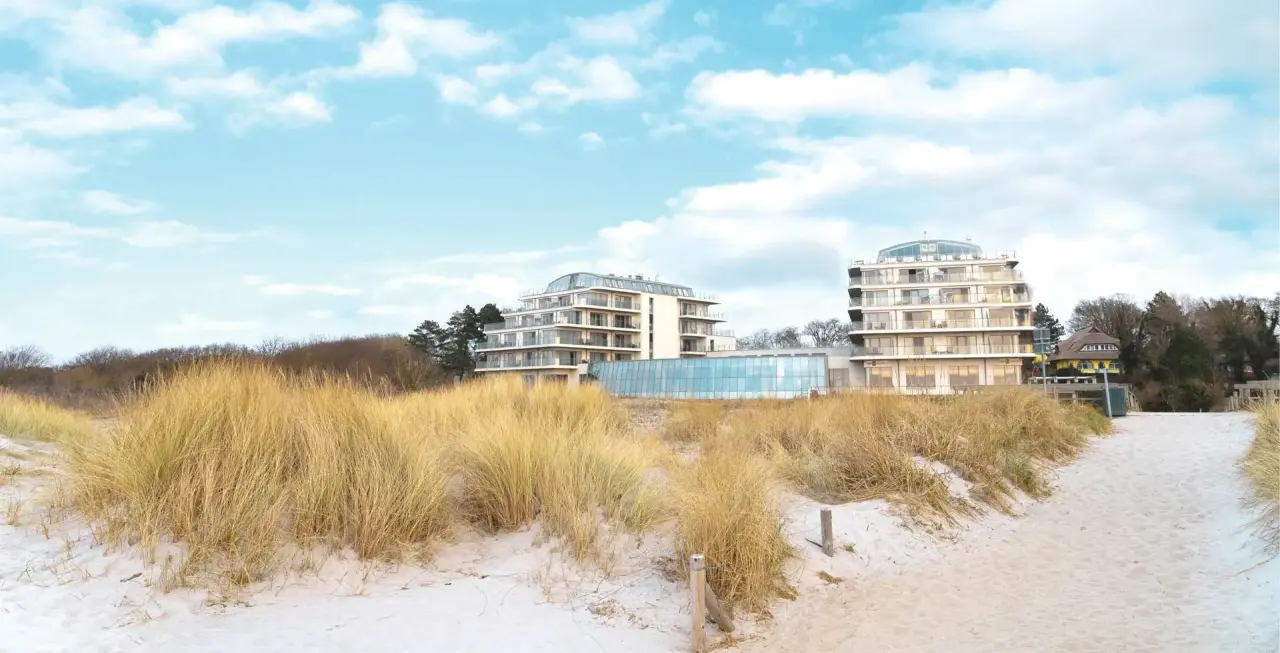 Das The Grand Ahrenshoop Hotel vom Strand aus gesehen, mit Dünengras im Vordergrund und blauem Himmel.