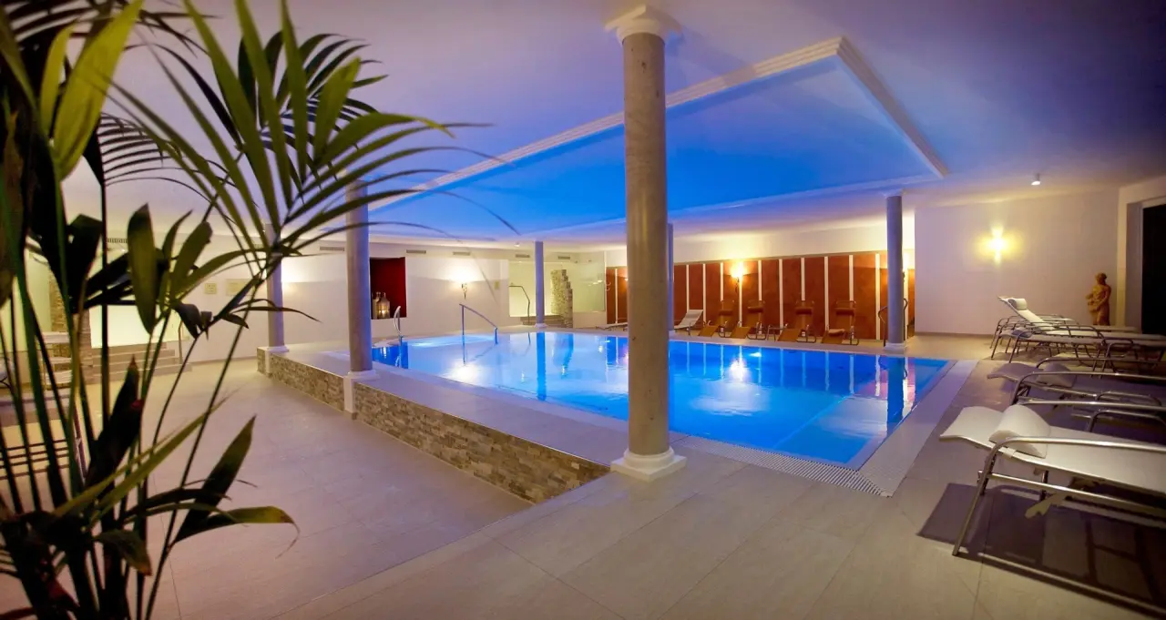 Beheizter Innenpool mit blauer Beleuchtung und Liegebereich im Wellnesshotel Rothfuss. Ideal zur Entspannung.