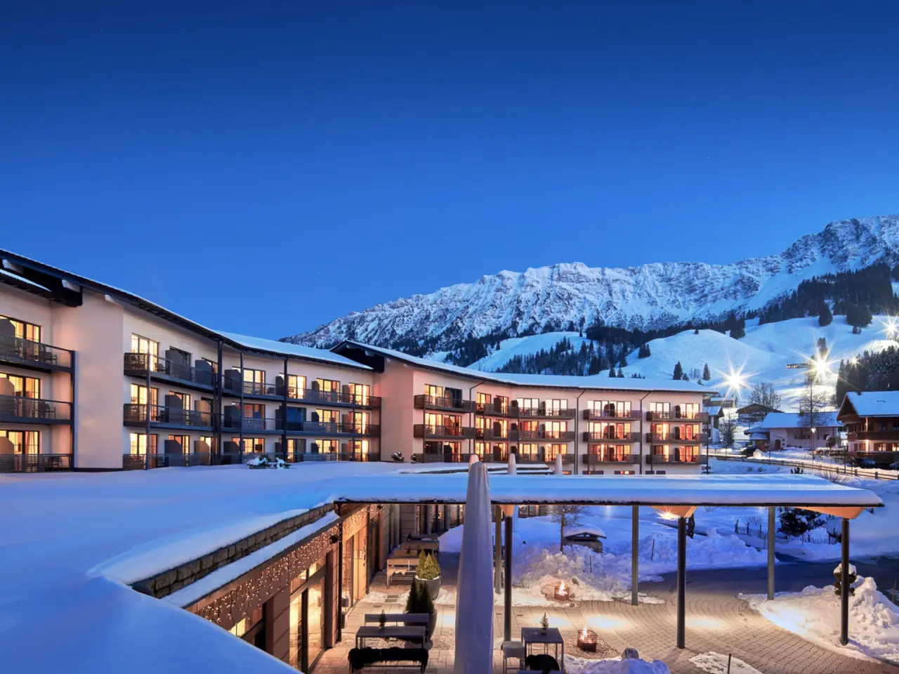 Panoramahotel Oberjoch im Winter bei Dämmerung, beleuchtete Fassade und verschneite Alpenkulisse.