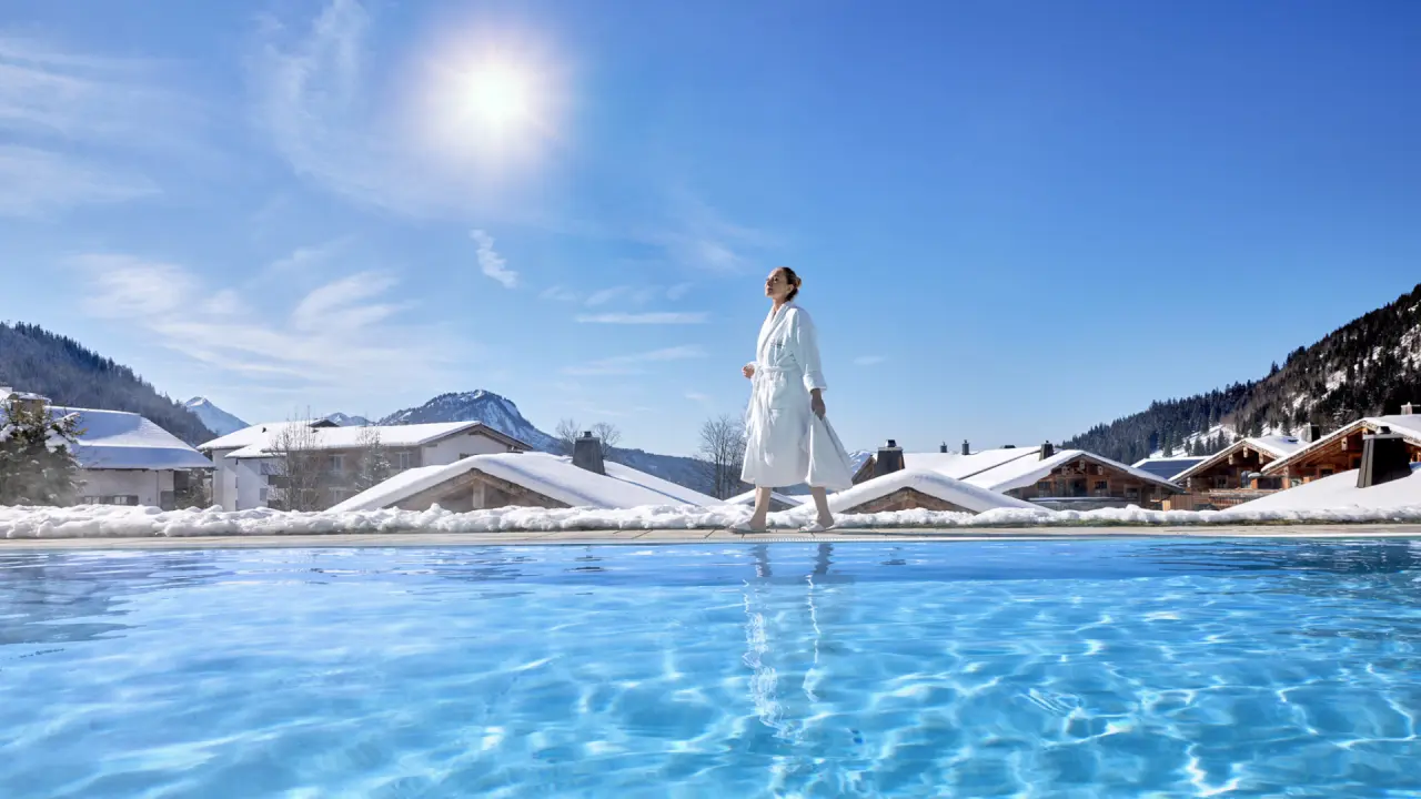 Infinity Pool mit Bergpanorama und Gast im Bademantel im winterlichen Panoramahotel Oberjoch.