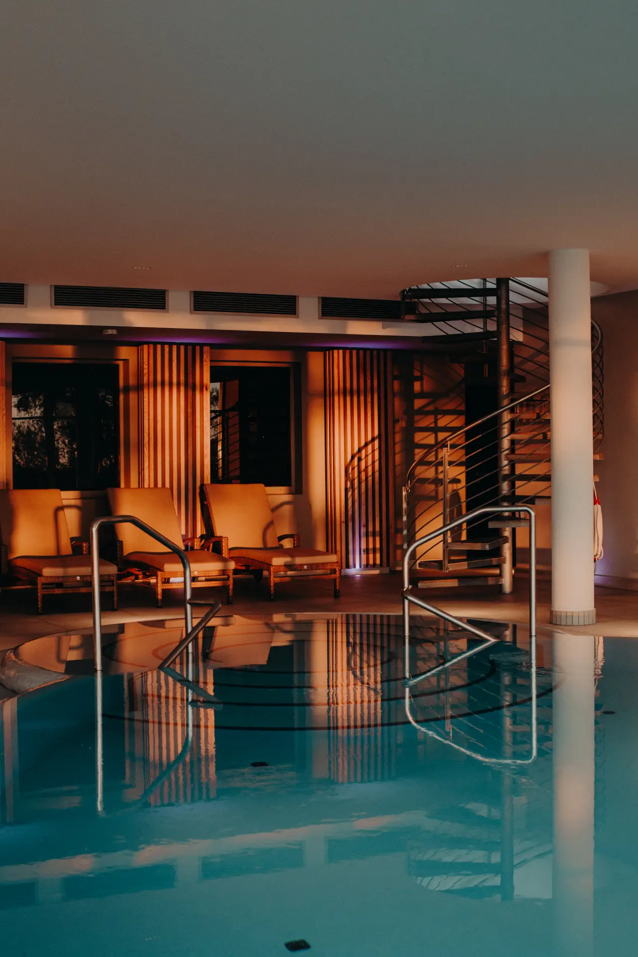 Stimmungsvoller Innenpool mit bequemen Liegen und Wendeltreppe im Wellnessbereich des Strandhotel Ostseeblick.