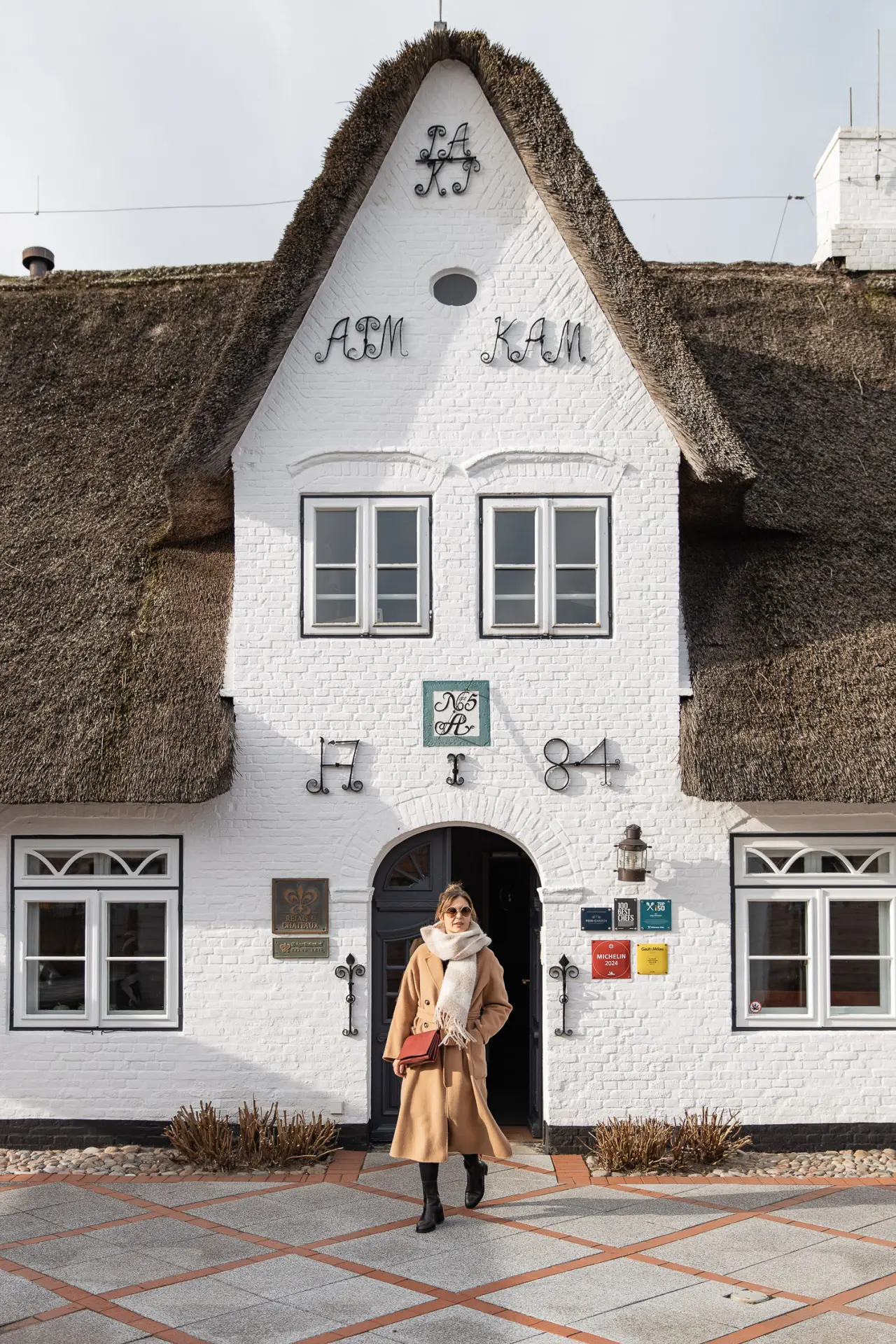 Eingang des Landhaus Stricker mit traditionellem Reetdach und weißer Backsteinfassade. Eine Person verlässt das Hotel.