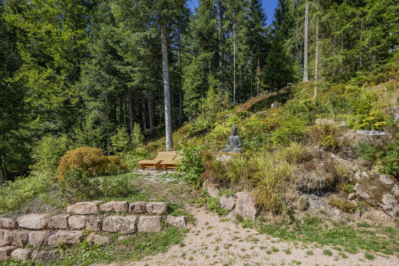 Ruhiger Meditationsbereich mit Buddha-Statue und Holzbank im Waldgarten des Hotel Langenwaldsee