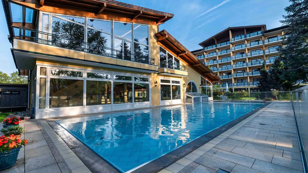 Aussenansicht des Kurhotel Zink mit grossem Aussenpool und moderner Architektur unter blauem Himmel.