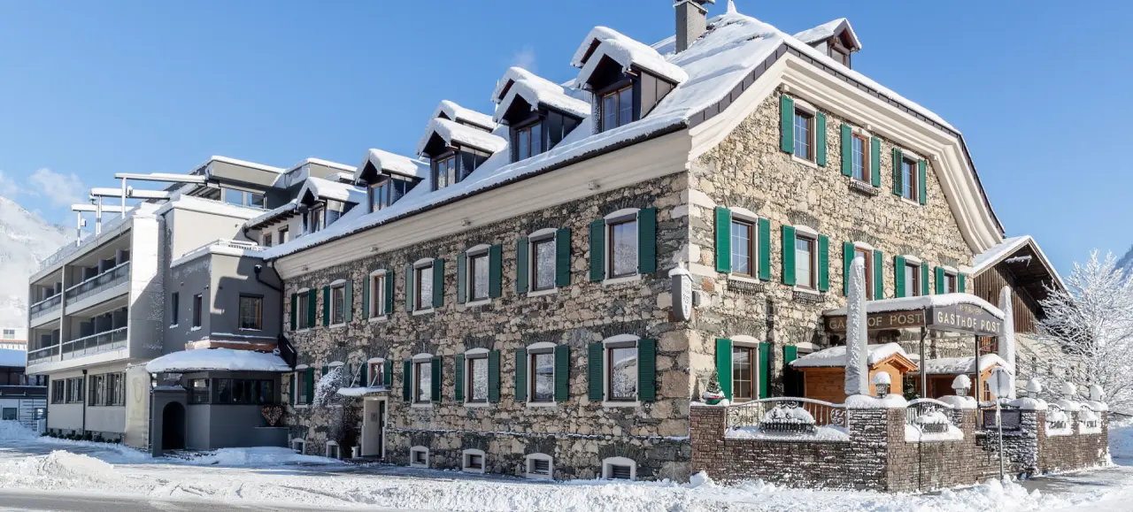 Winterliche Aussenansicht des traditionellen Gasthof Hotel Post mit verschneitem Dach und Bergkulisse.