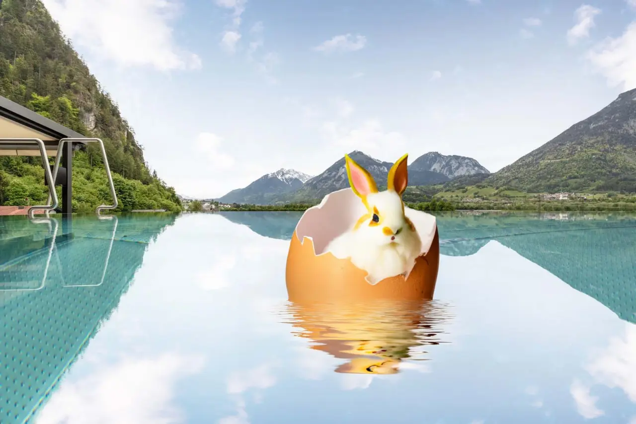 Infinity Pool des Gasthof Hotel Post mit Alpenpanorama. Ein Osterhase im Ei schwimmt im klaren Wasser.