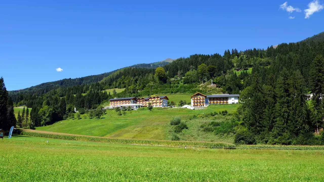 Hotel Glocknerhof in den Alpen, umgeben von grünen Wiesen und Wäldern unter blauem Himmel.