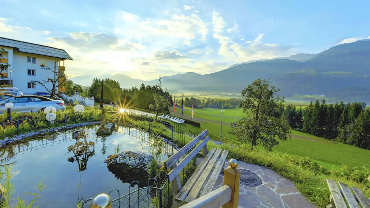 Malerische Aussenansicht des Hotel Glocknerhof bei Sonnenaufgang mit Teich und Alpenpanorama.