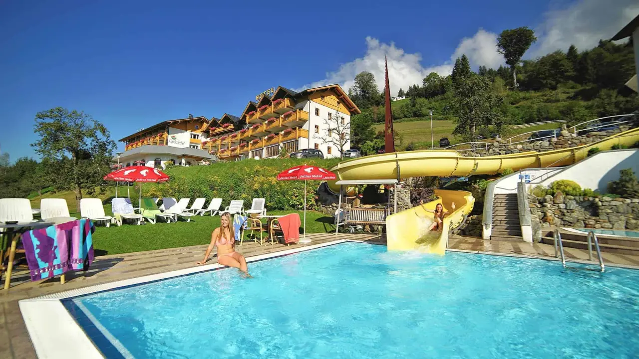 Sonniger Aussenpool mit gelber Wasserrutsche und Liegewiese am Hotel Glocknerhof. Gäste geniessen den Badespass in den Bergen.