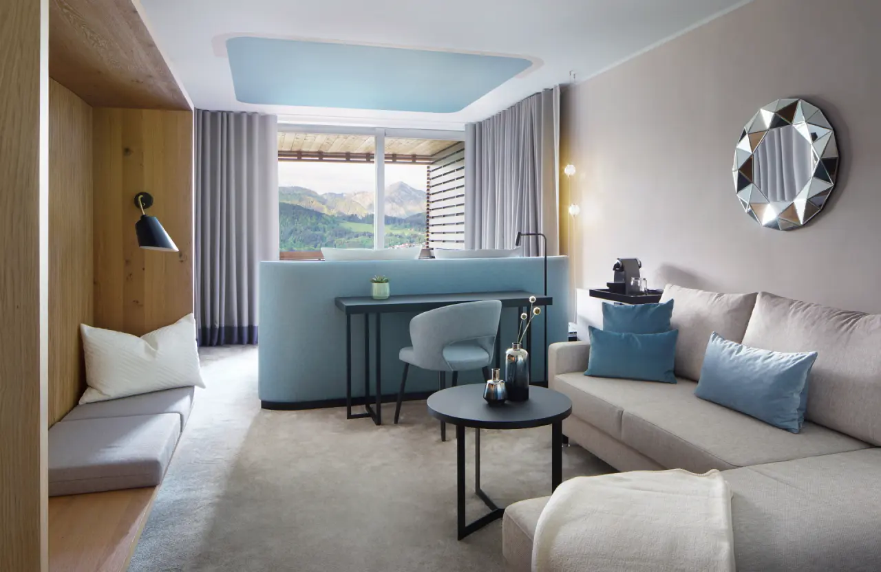 Modernes Hotelzimmer im DAS TEGERNSEE mit stilvollem Design, gemütlicher Sitzecke und atemberaubendem Blick auf die bayerischen Alpen.