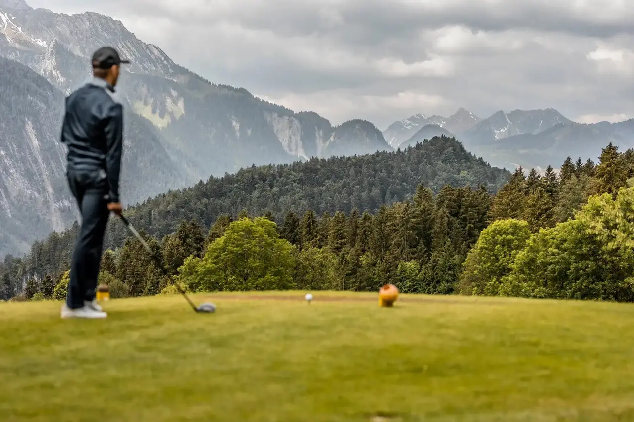 Golfer auf dem Abschlag mit Blick auf die majestätischen Alpen im TRAUBE BRAZ Alpen.Spa.Golf.Hotel.