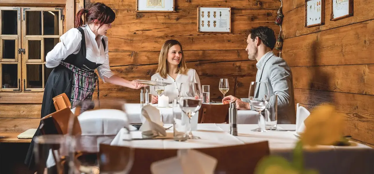 Gastfreundschaft im Restaurant des TRAUBE BRAZ Alpen.Spa.Golf.Hotel mit Servicekraft und lächelnden Gästen in gemütlicher Atmosphäre.
