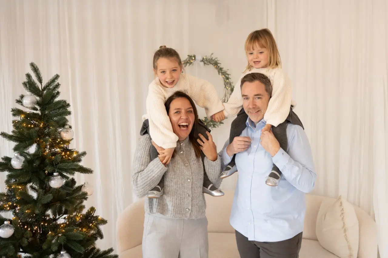 Fröhliches Familienfoto mit Kindern auf den Schultern vor einem Weihnachtsbaum im Hotel Das König Ludwig Inspiration SPA.