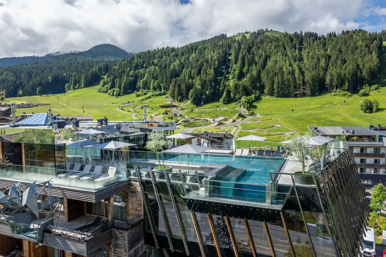 Dachterrassen-Infinity-Pool des Salzburger Hof Leogang mit Blick auf die umliegende Berglandschaft und grüne Wiesen.