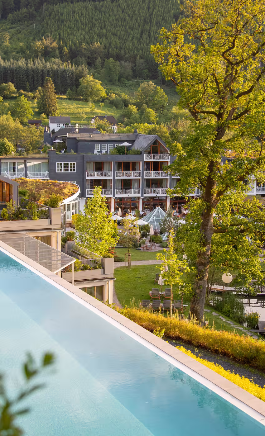 Romantikhotel Deimann in Schmallenberg-Winkhausen – Infinity-Außenpool mit Hotelgebäude und Grünanlage | Wellnesshotel Sauerland