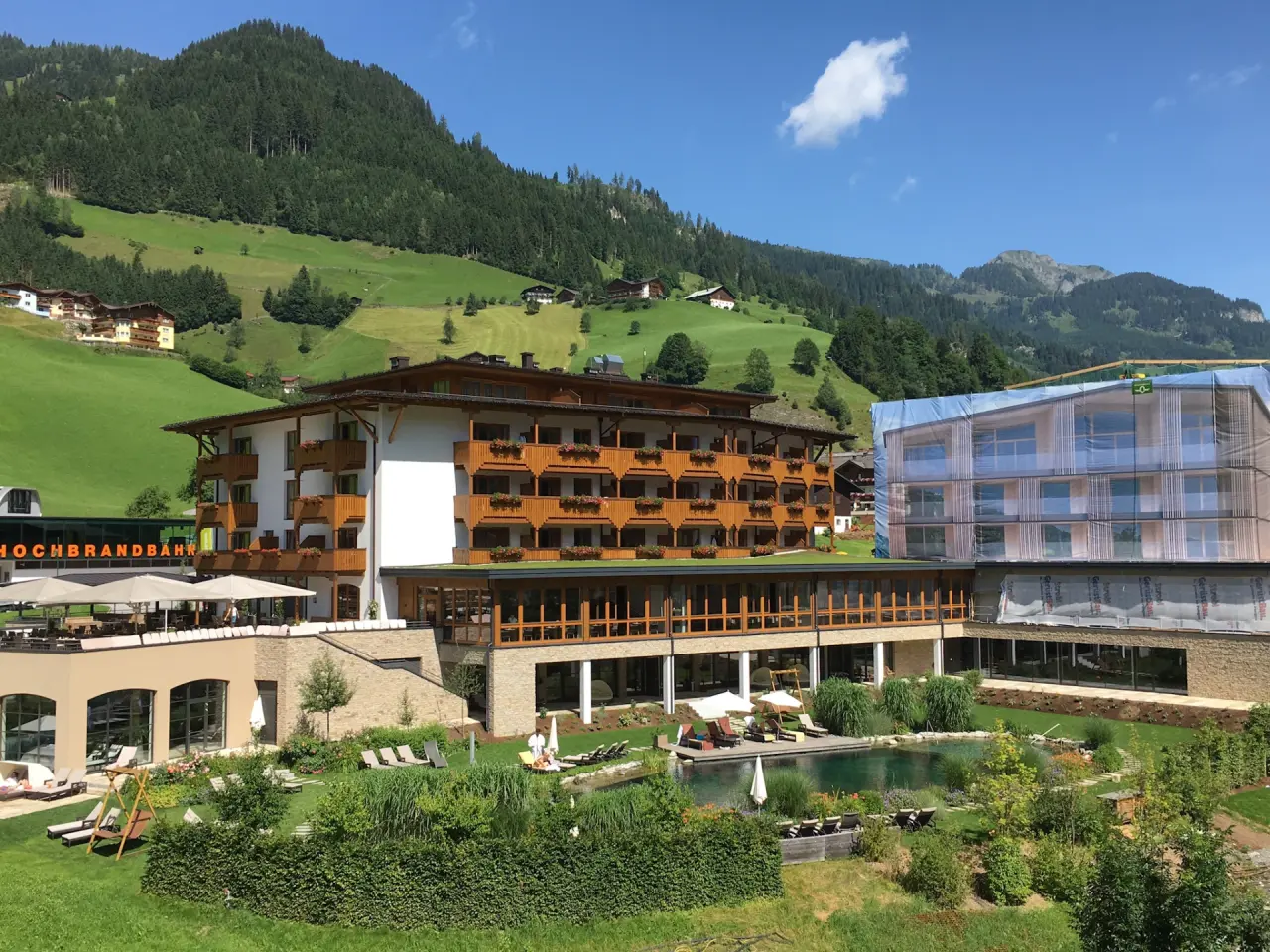 Aussenansicht des Hotel Nesslerhof mit Naturpool, Liegewiese und Alpenpanorama unter blauem Himmel.