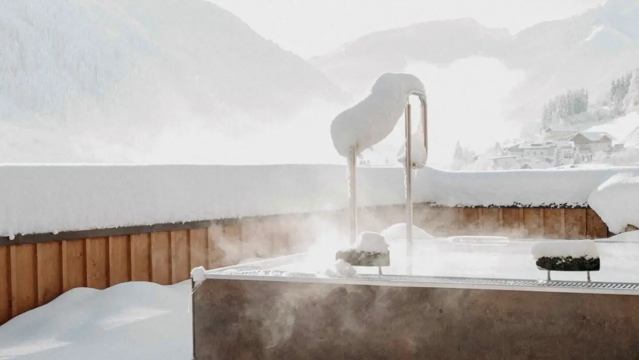 Beheizter Outdoor-Whirlpool im Schnee mit Bergblick im Hotel Nesslerhof. Dampf steigt auf, umgeben von Winterlandschaft.