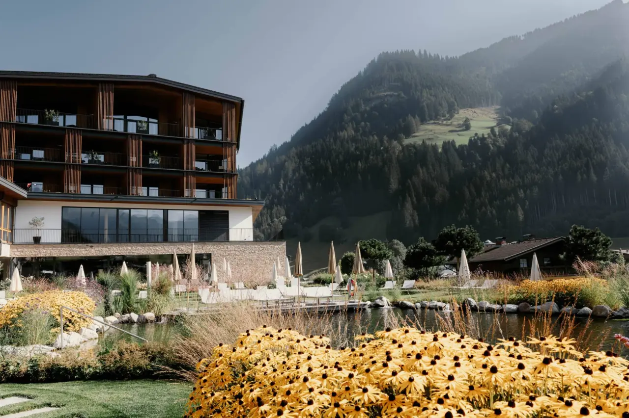 Aussenansicht des Hotel Nesslerhof mit Natur-Badeteich, Liegewiese und majestätischem Alpenpanorama.