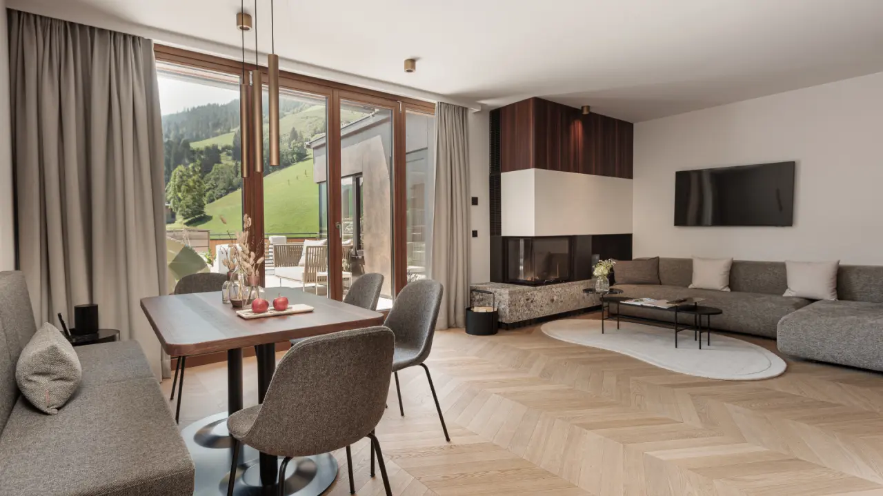 Geräumige Suite im Hotel Nesslerhof mit Kamin, Essbereich und Panoramablick auf die Berge und grüne Wiesen.