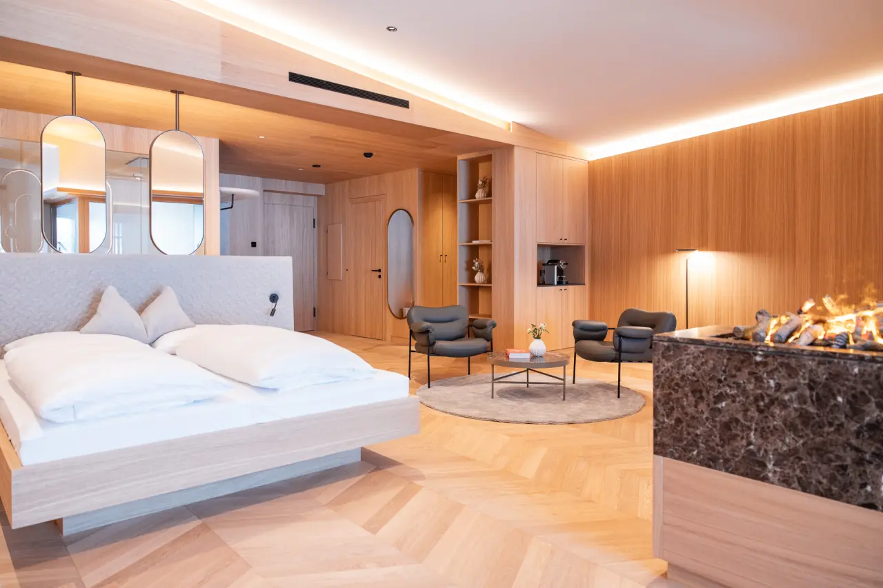 Luxuriöses Hotelzimmer im Hotel Nesslerhof mit Doppelbett, gemütlicher Sitzecke und modernem Kamin für entspannte Stunden.