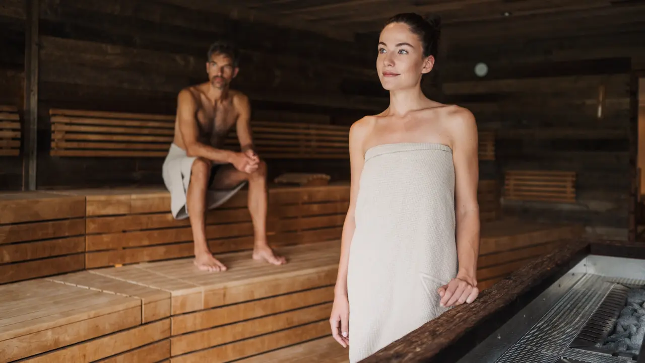 Ein Paar entspannt in der stilvollen Holzsauna des Hotel Nesslerhof. Perfekte Wärme und Ruhe im Wellnessbereich.